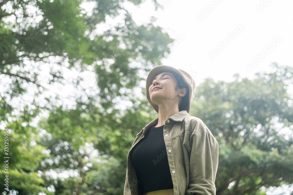 Young asian woman traveller relaxing in nature forest background. Happy Beautiful woman standing middle of a lot of tree. Breathing the fresh air on her vacation weekend holiday trip.