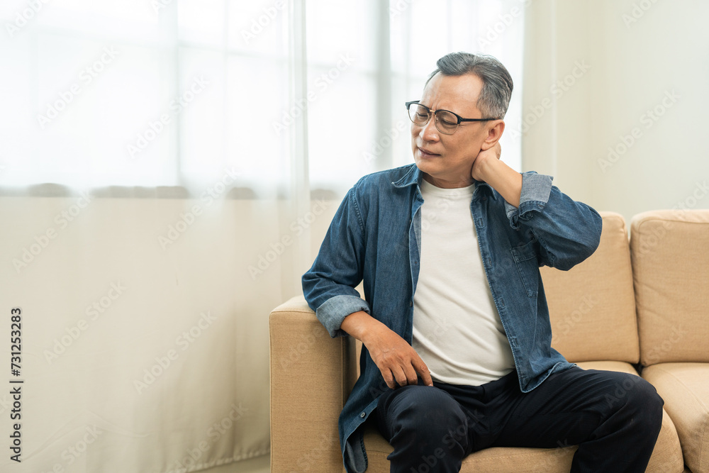 Old man senior has problem with structural posture He had neck and shoulder pain. Mature Massaged his neck and shoulders for relief. reduce muscle tension. Sitting on sofa couch in living room