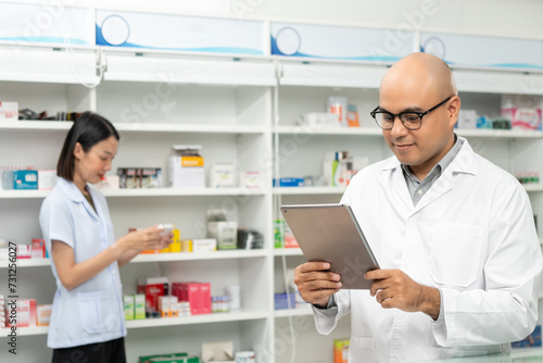 Professional asian man pharmacist checks inventory arrangement of medicine in pharmacy drugstore. Male Pharmacist wearing uniform standing near drugs shelves counter prescription to customers