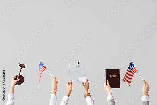 Hands holding ballot box, law book, USA flags and judge's gavel on white background. Election concept