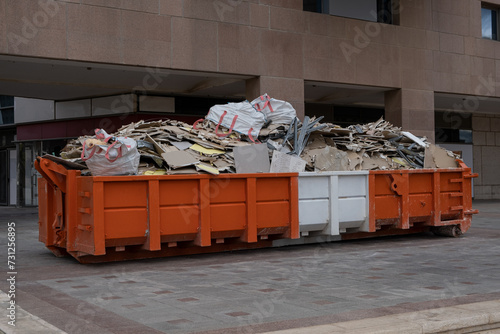 huge heap on metal Big  Overloaded dumpster waste container filled with construction waste, drywall and other rubble near a construction site.
