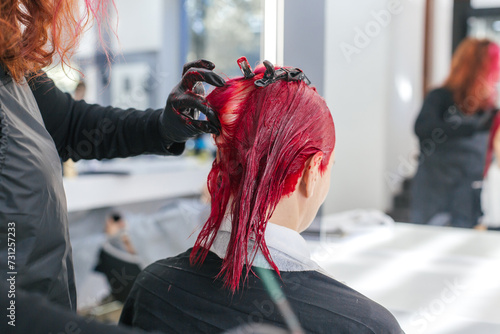 Photos hairdresser colorist dyes a client's hair red in a hair salon.