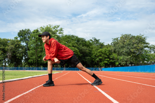 Young asian man wearing sportswear running outdoor. Portraits of Indian man stretching leg before running on the running track at sport stadium. Training athlete work out at outdoor concept.