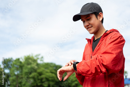 Young man wearing sportswear red jacket using Smart Watch Showing Heart Rate Monitor. Technology for health and sport mode. Exercise and take statistics to develop your potential at sport stadium