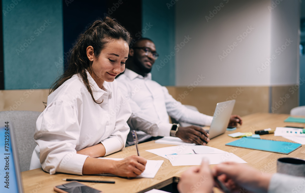 Smiling female employee writing notes during meeting Smiling female employee writing notes during meeting
