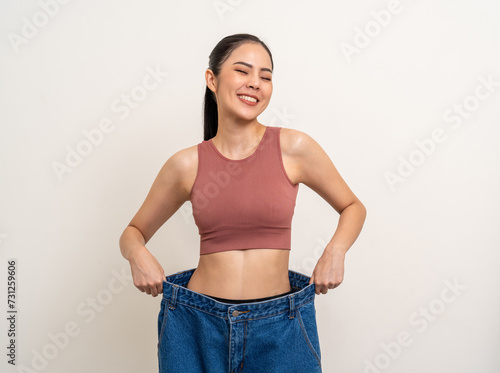 Young asian woman thin slender abdomen waist wearing old big jean after her success weight loss diet session. Care about eating and workout exercise for slim fit and firm good shape