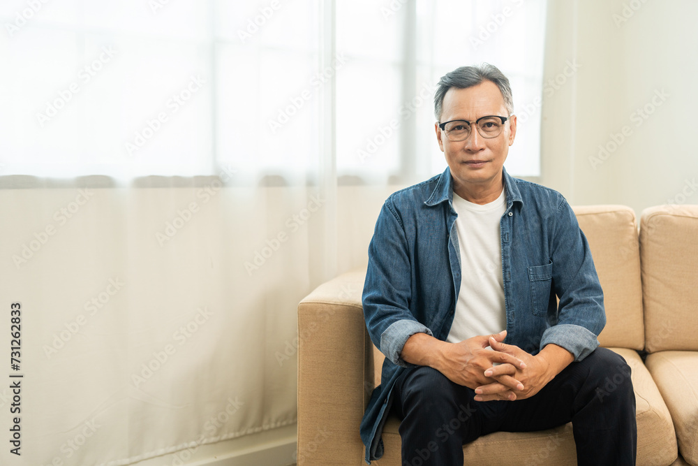 Handsome asian mature old man sitting on sofa couch in living room at home. Happy Portrait of cheerful smiling senior asian man relax in the house. Mature People and lifestyle Handsome asian mature old man sitting on sofa couch in living room at home. Happy Portrait of cheerful smiling senior asian man relax in the house. Mature People and lifestyle