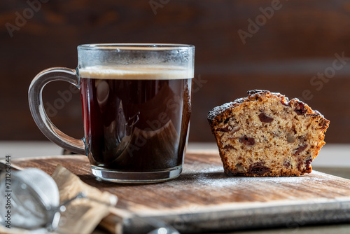 Delicious muffin with red cherries, walnuts and glass cup of black coffee on a wooden table, closeup. Fresh cupcake and coffee for breakfast