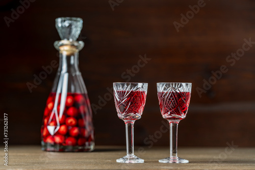 Homemade cherry brandy in two glasses and in a glass bottle on a wooden background, closeup
