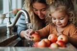 A mother tenderly cleanses the apples in her kitchen sink while her curious child watches on, the scene capturing the essence of domesticity and familial love