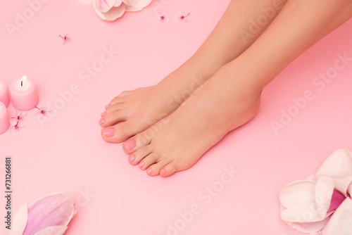 Well-groomed female feet with flowers and candles on a pink background.