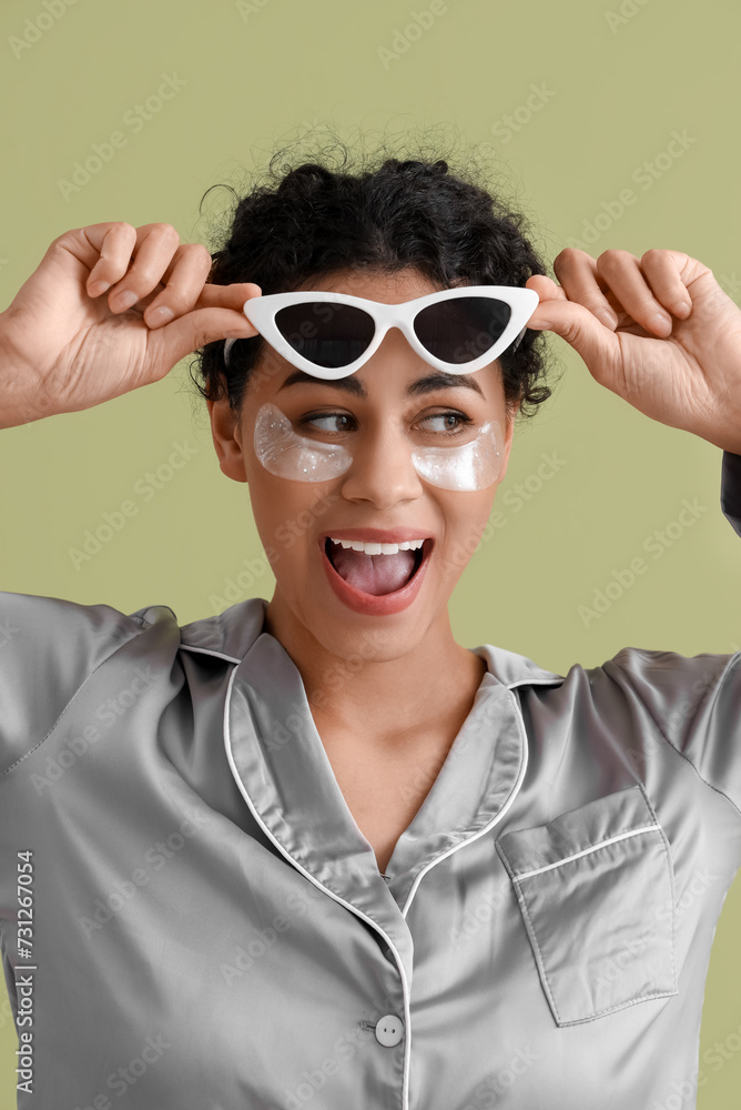 Young African-American woman with under-eye patches and sunglasses on green background, closeup