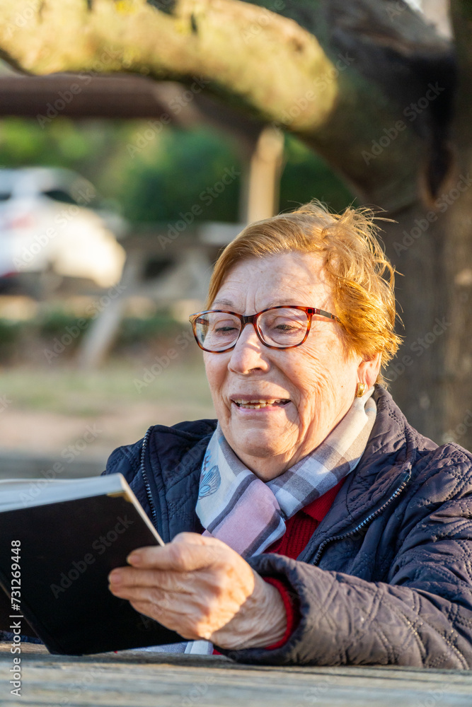 Older woman enjoying reading a book sitting on a bench in the park at sunset Older woman enjoying reading a book sitting on a bench in the park at sunset