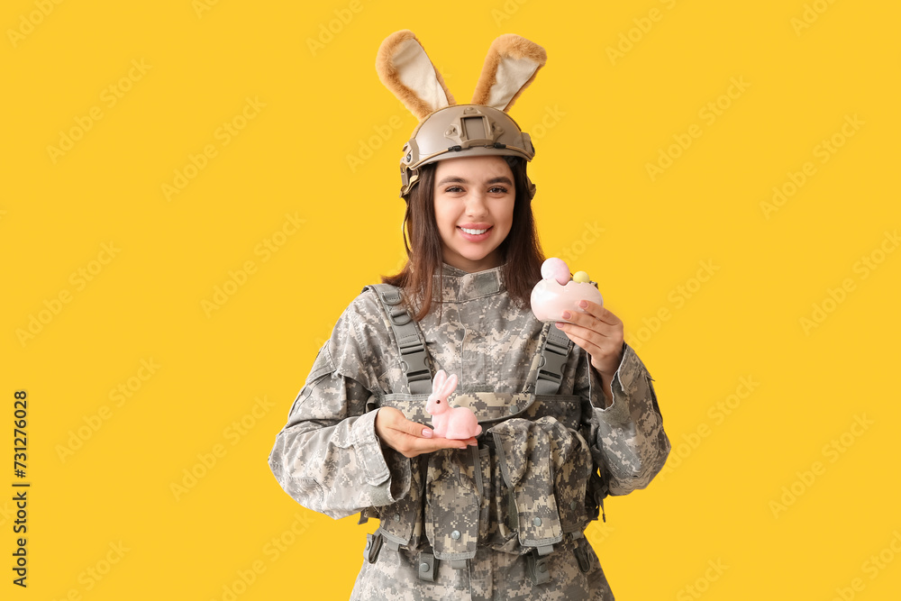 Female soldier in bunny ears with Easter rabbit and eggs on yellow background Female soldier in bunny ears with Easter rabbit and eggs on yellow background