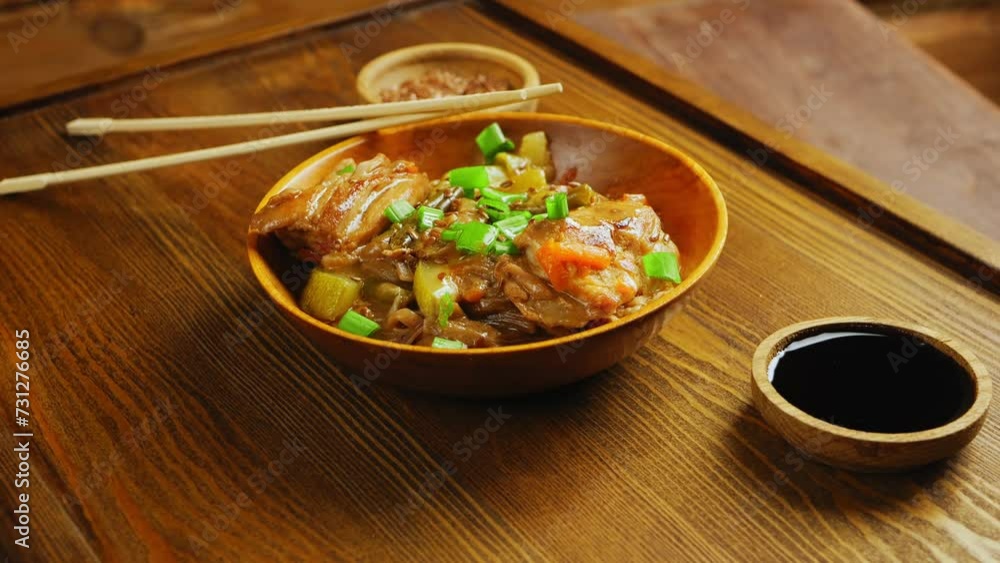 Soba noodles with chicken and vegetables in a wooden plate next to soy sauce and sesame sticks rotating in a circle. Close-up. Soba noodles with chicken and vegetables in a wooden plate next to soy sauce and sesame sticks rotating in a circle. Close-up.