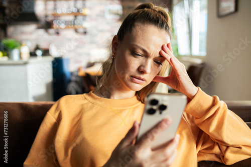 Worried young woman using smartphone on home sofa photo