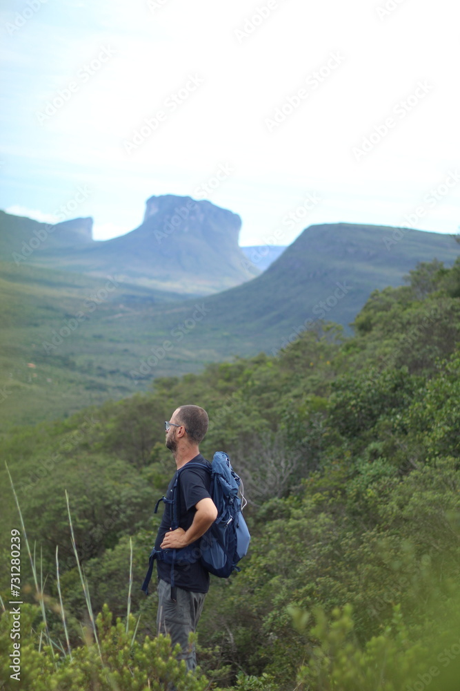 homem de mochila nas costas em trilha na Chapada Diamantina, Bahia, com motanhas ao fundo