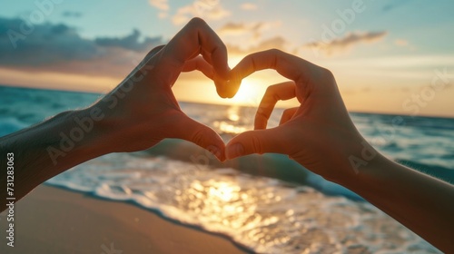 A male and female couple put their hands together in a heart shape. At the sandy beach by the sea The sun is about to set.