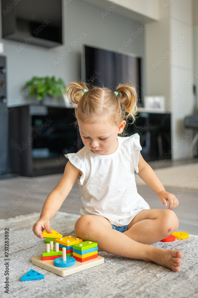 Cute caucasian little girl playing on the floor at home with eco wooden toys. Montessori toy. The child playing educational games. Cute caucasian little girl playing on the floor at home with eco wooden toys. Montessori toy. The child playing educational games.