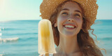 Joyful Woman with Ice Cream at the Beach. Smiling young woman wearing a straw hat enjoys a fruit ice cream popsicle on a sea sunny beach backdrop.
