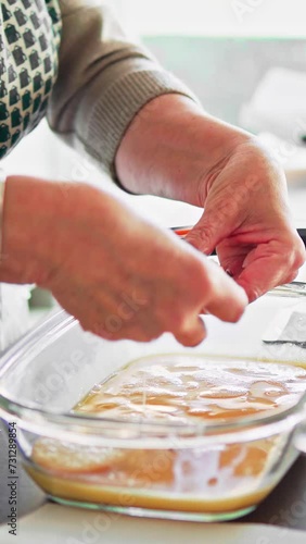 Video vertical de las manos de una mujer rebozando torrijas españolas de Semana Santa con la receta tradicional en una cocina actual.	 photo
