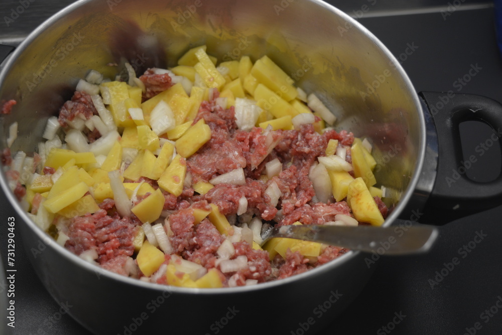 Cooking a delicious and healthy meal, minced meat with onions and sliced potatoes is located in a large metal pot.