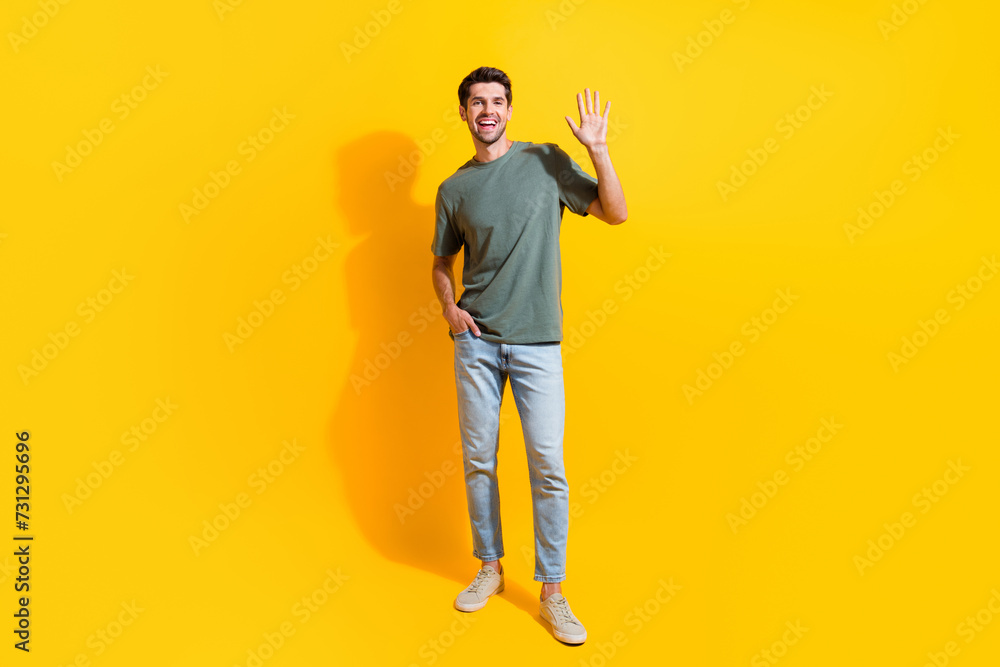 Full length photo of good mood friendly guy wear khaki t-shirt waving arm hi isolated yellow color background Full length photo of good mood friendly guy wear khaki t-shirt waving arm hi isolated yellow color background