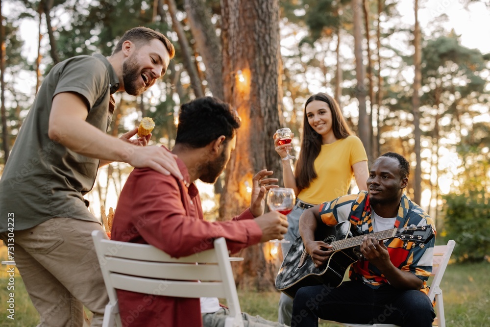 Multiracial group of friends, African man playing guitar around happy friends drinking wine Multiracial group of friends, African man playing guitar around happy friends drinking wine
