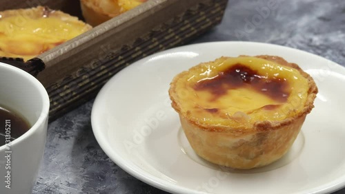 The hand of a baker, cook or waiter places a fresh and hot crispy puff pastry pie with egg custard on the table in a cafe on a white plate. Portuguese dessert Pastel de Nata or Pastel de Belem.