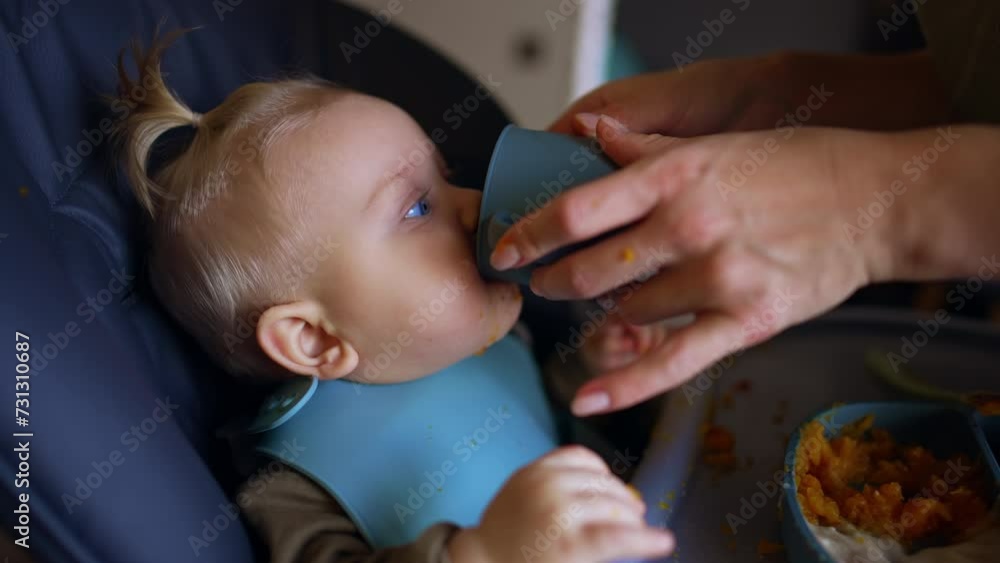 Unrecognized woman giving a cup with a drink to her baby. Little kid coughs after drinking. Close up. Unrecognized woman giving a cup with a drink to her baby. Little kid coughs after drinking. Close up.