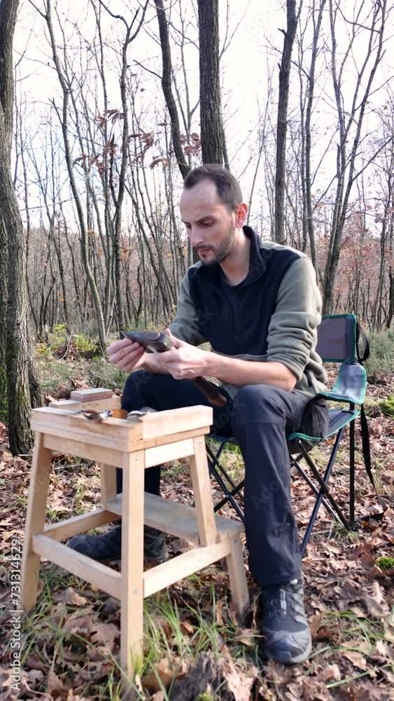 Carpenter checks the sharpness of an axe and starts to sharpen it. He sits on a camping chair in a forest. Carpenter checks the sharpness of an axe and starts to sharpen it. He sits on a camping chair in a forest.