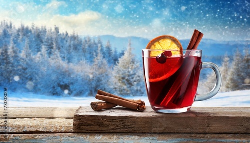 a glass of mulled red wine with cinnamon on old rustic wooden plank against blue background with winter landscape