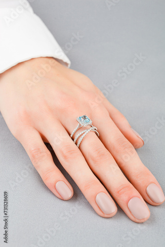 Beautiful female hand with gold ring with diamonds and aquamarine on gray background