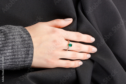 Beautiful female hand with gold ring with diamonds and emerald on gray background © Minakryn Ruslan 