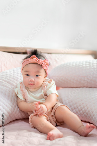 Asian baby infant girl with pink hair bow sit on bed at morning time.