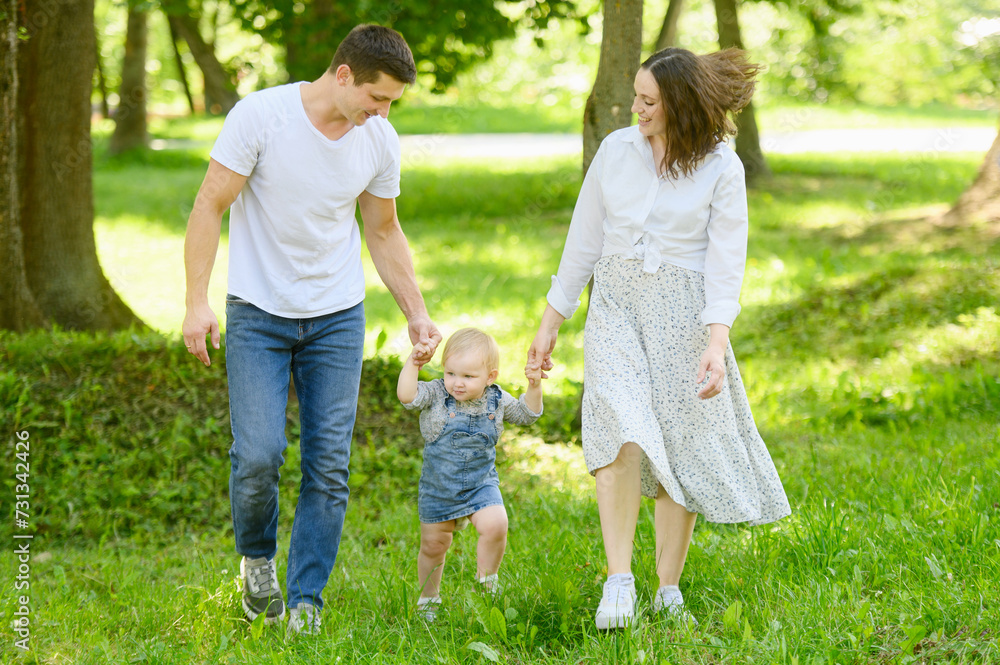 Child walks in the park on the grass holding hands with his parents, learns to walk, take his first steps.Happy family