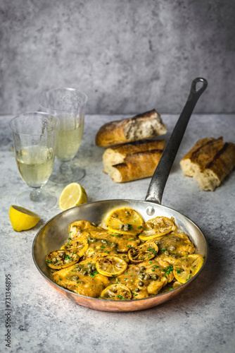 Chicken, lemon slices and capers in a copper skillet, with bread and white wine photo