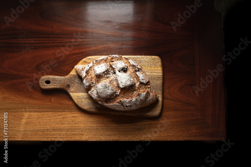 Rustic bread loaf on wooden chopping board on antique wood.