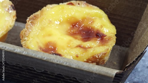 A baker's or cook's hand places a fresh and hot crispy puff pastry pie with egg custard into a paper package in a cafe. Traditional Portuguese dessert Pastel de Nata or Pastel de Belem.