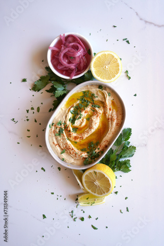 Chickpea hummus served with olive oil, pickled red onion, lemons, and flatbread on a white marble table background. Minimal layout flatlay. photo