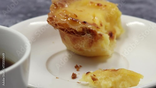 Eating with a dessert fork a fresh and hot crispy puff pastry pie with egg custard on a white plate at breakfast in a cafe with coffee. Portuguese dessert Pastel de Nata or Pastel de Belem.