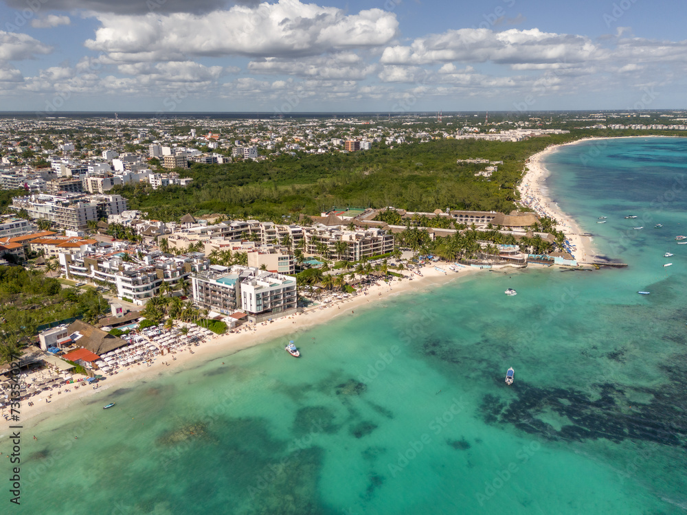 Aerial drone view of beach with blue transparent Caribbean Sea with buildings and large green vegetation area on a beautiful day with cloudy blue sky in Playa del Carmen 
