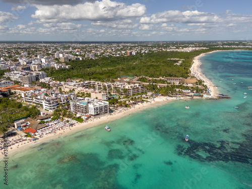 Fototapeta Naklejka Na Ścianę i Meble -  Aerial drone view of beach with blue transparent Caribbean Sea with buildings and large green vegetation area on a beautiful day with cloudy blue sky in Playa del Carmen 