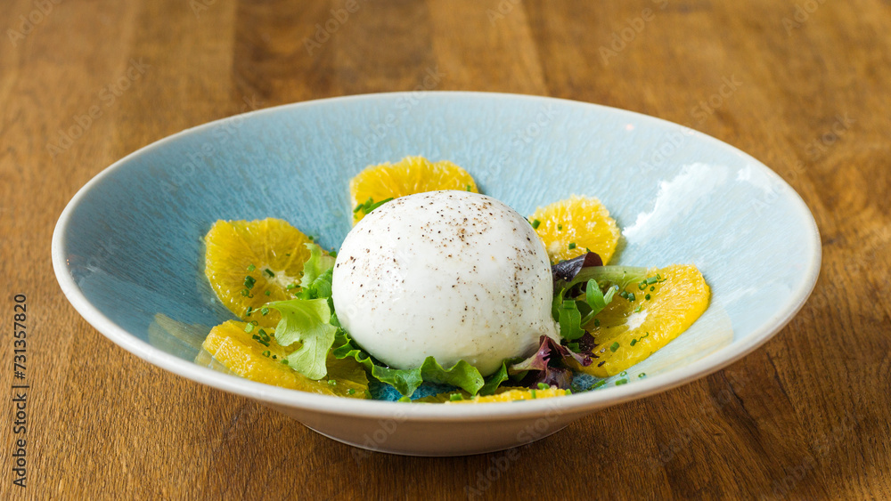 Burrata grapefruit salad in a dish on a wooden table in a restaurant Burrata grapefruit salad in a dish on a wooden table in a restaurant
