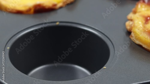 A hand takes out a fresh and hot pie made of crispy puff pastry with egg custard from a special baking dish. Traditional Portuguese dessert Pastel de Nata or Pastel de Belem. National delicacy.