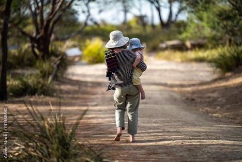 Mother with baby in a carrier on her chest on a hike, taking a bush walk in Summer in a national park