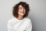 Portrait of beautiful young woman with curly hair laughing on gray background