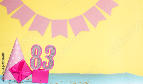 Date of birth for a girl 83. Copy space. Birthday in pink shades with a yellow background. Decorations with numbered candles and a gift box. Anniversary card for a woman