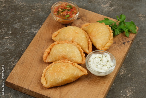 Homemade Stuffed Chicken Empanadas Served with Salsa Sauce on a Background