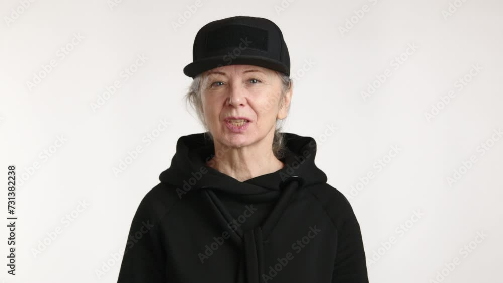 A woman wearing a black hat and hoodie is playfully blowing a kiss while her jaw and sleeve are partially covered. A woman wearing a black hat and hoodie is playfully blowing a kiss while her jaw and sleeve are partially covered.